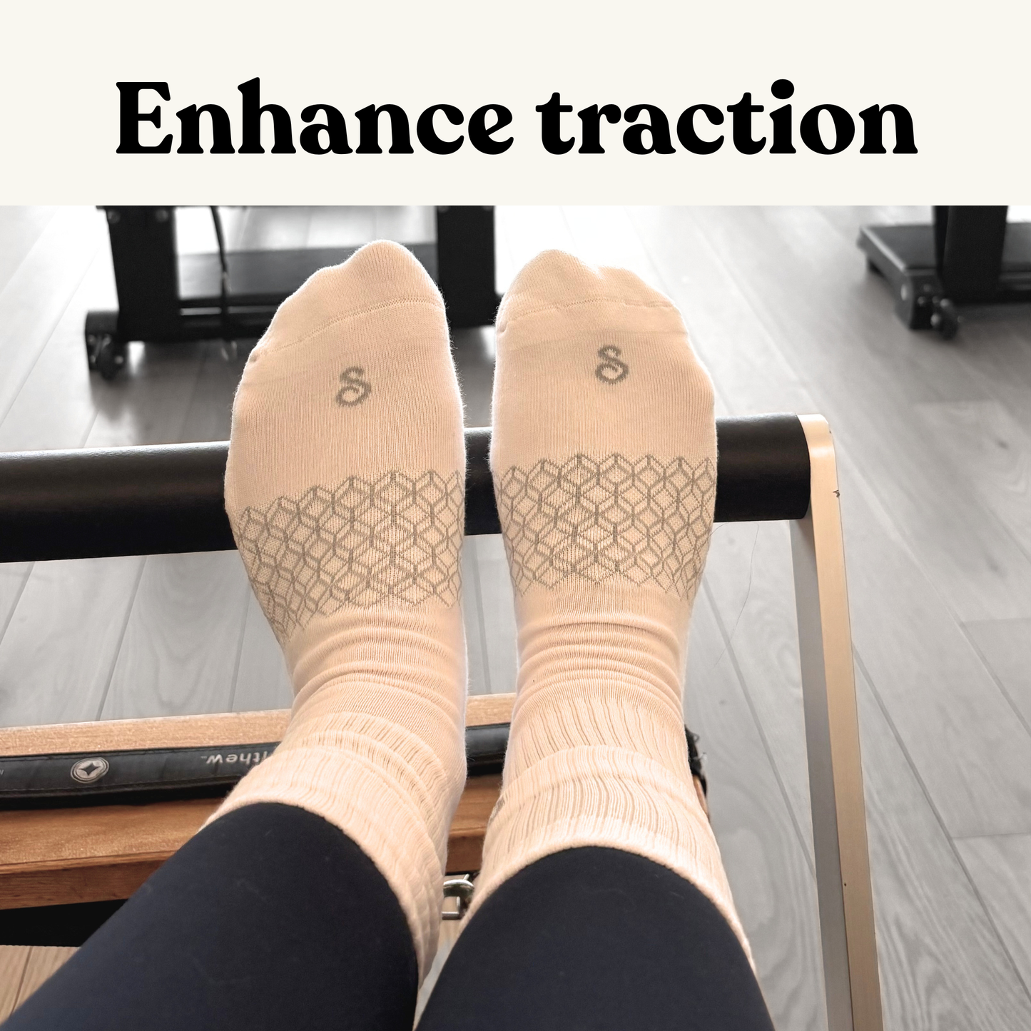 A person wearing hipSwan Flow Crew white grip socks with a geometric pattern and the text 'Enhance traction' at the top, sitting on a Pilates reformer exercise machine.