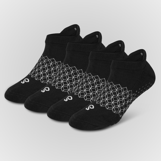 Four black low-cut ankle grip socks arranged in a fan shape on a light gray background. Each sock features a white geometric honeycomb pattern around the ankle area and a small white logo near the toe.