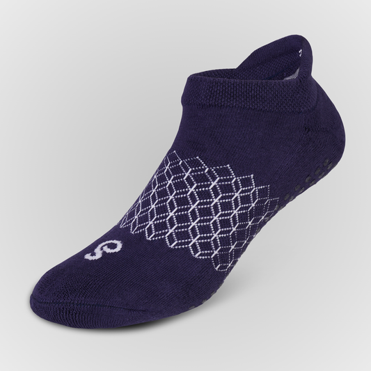 A single navy blue low-cut athletic grip sock with a white dotted geometric pattern on the side and a stylized white logo on the toe, shown against a light gray gradient background.